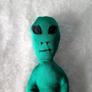 May include: A green plush alien toy with black eyes and a stitched-on mouth.