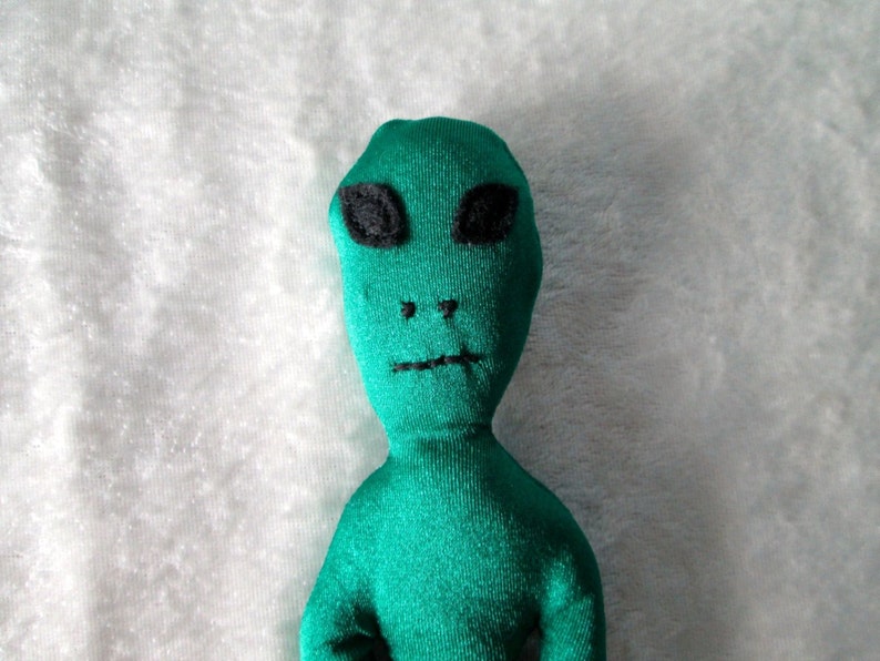 May include: A green plush alien toy with black eyes and a stitched-on mouth.