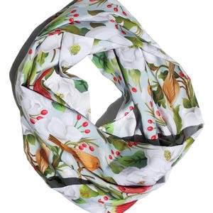 May include: A light blue infinity scarf with a floral print featuring white flowers, green leaves, red berries, and brown birds.