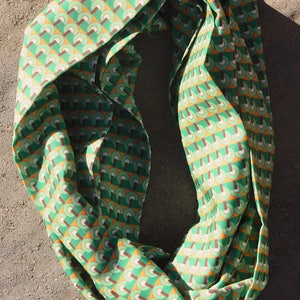 Könnte beinhalten: Ein grüner und orangefarbener gemusterter Infinity-Schal. Das Muster besteht aus sich wiederholenden geometrischen Formen.