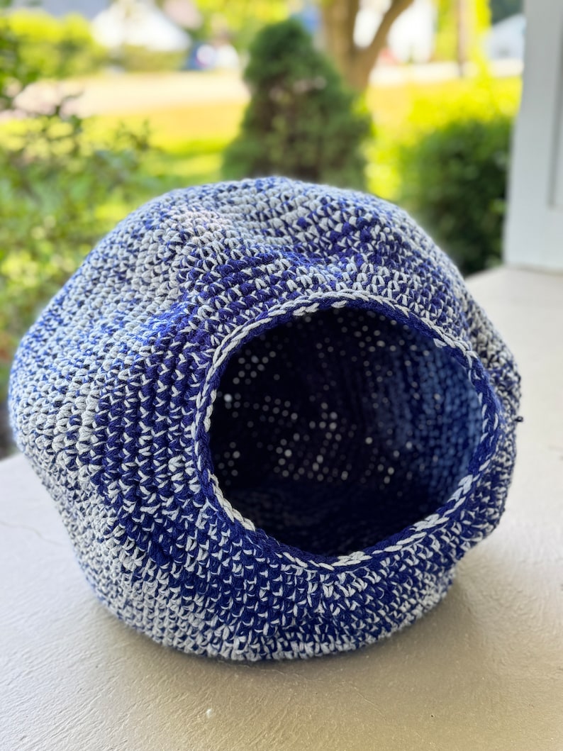 May include: A blue and white crocheted pet bed with a round opening. The bed is made of a soft, textured yarn.