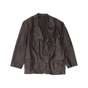 May include: A dark brown leather blazer featuring a notched lapel, long sleeves, and a two-button front closure. The jacket includes two horizontal welt pockets at the waist and a smooth, dark interior lining visible at the open collar area.