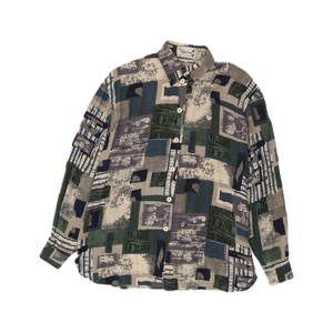 Puede incluir: Una camisa de manga larga con botones y un estampado geométrico y abstracto de bloques en tonos verde oscuro, azul marino, gris y crema. La camisa cuenta con un cuello estándar y una tapeta frontal con botones de color claro.