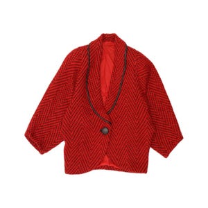 May include: A red blazer featuring a black chevron pattern, a shawl collar with black trim, and a single black button closure. The garment has long sleeves and a solid red interior lining, showcasing a structured design with a textured fabric finish.