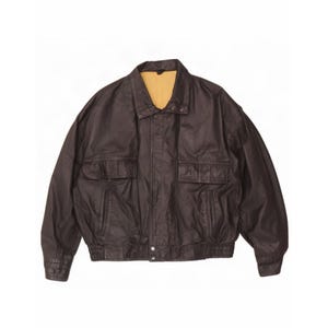 May include: A dark brown leather jacket featuring a pointed collar, a front zipper closure with a snap button placket, two large flap pockets on the chest, two side slit pockets, and an elasticized waistband with matching cuffs and a tan lining.