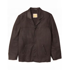 May include: A dark brown leather jacket featuring a notched collar, a front button closure with four visible buttons, and two slanted welt pockets at the waist. The interior neckline displays a small rectangular label with yellow text.