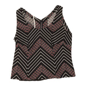 May include: A sleeveless black top featuring a white chevron pattern and small floral accents in red and white. The garment has a V-neckline and a central vertical seam running down the front, with a visible zipper closure at the back neckline.