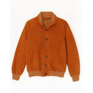 May include: A burnt orange jacket featuring a ribbed collar and cuffs, a button-down front closure with dark buttons, and two side pockets. The jacket has a soft, matte texture and long sleeves, providing a structured yet comfortable appearance.