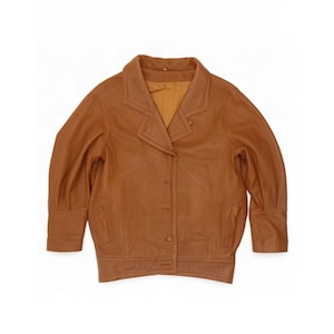 May include: A tan leather jacket featuring a wide notched collar, long sleeves with cuffed wrists, and a front button closure. The jacket includes two vertical slit pockets on the front and a smooth, matching tan interior lining visible at the neckline.