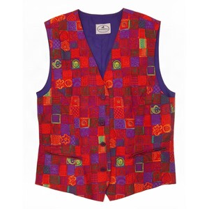 Può includere: Un gilet senza maniche con un vivace motivo patchwork di quadrati rossi, viola e arancioni con vari disegni a linee. Il capo presenta uno scollo a V, una chiusura frontale a quattro bottoni, due tasche a filetto e una fodera color viola.