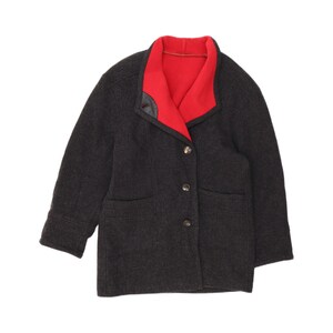 May include: A charcoal grey wool-blend jacket featuring a vibrant red inner lining and collar. The jacket has long sleeves, two front pockets, and a three-button closure down the front. The collar is wide and folded, revealing the bright red interior.