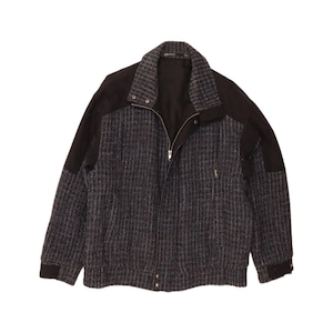May include: A zip-up jacket featuring a dark gray and black textured tweed pattern on the front and sleeves, contrasted by solid black panels on the shoulders and collar. The garment includes a full-length front zipper and ribbed cuffs.