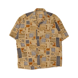 May include: A short-sleeve button-down shirt featuring a tan, brown, and dark grey geometric pattern. The design includes various squares, rectangles, and grid motifs arranged in an abstract layout across the fabric, with a standard collar.