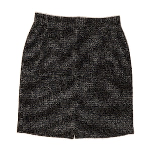 May include: A knee-length skirt featuring a dark black and white tweed fabric with a textured, woven appearance. The skirt has a straight silhouette, a high waistband, and a small vertical slit at the center of the bottom hemline.