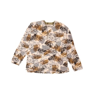 Könnte beinhalten: Ein langärmliges Hemd mit cremefarbenem Hintergrund und einem Muster aus braunen, grauen und schwarzen Pinselstrichen und kartenartigen Designs. Das Hemd hat einen runden Halsausschnitt mit grünem Besatz.