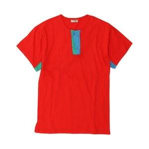 Puede incluir: Una camiseta roja de manga corta con un diseño de bloques de color contrastantes en la tapeta y los puños. La tapeta presenta una franja vertical de tela verde y azul. La camiseta tiene cuello redondo y cierre de botón.