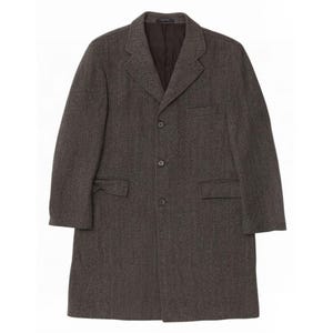 May include: A dark brown overcoat featuring a subtle herringbone pattern, a notched lapel, and a three-button front closure. The coat includes two side flap pockets, one chest pocket, and a dark interior lining, providing a structured silhouette.