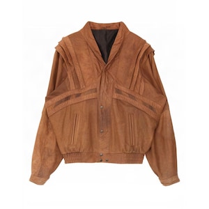 May include: A tan leather jacket featuring a shawl collar, structured shoulder panels with vertical pleats, and horizontal stitched detailing across the chest. The jacket includes two vertical slit pockets, a dark brown interior lining, and a ribbed hem.