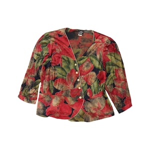 May include: A long-sleeved button-down blouse featuring a vibrant floral pattern with large red and green leaves against a black background. The garment has a V-neckline, a light-coloured trim along the front opening, and five small gold-toned buttons.