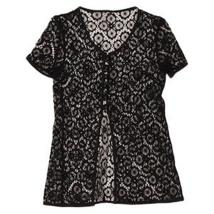May include: A black short-sleeved top featuring an intricate, repeating circular lace pattern throughout the garment. The piece has a V-neckline and a central vertical placket with small buttons, creating a semi-sheer, open-weave texture.