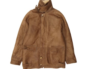 May include: A brown leather jacket featuring a high collar, long sleeves, and a front button closure. The jacket includes two front flap pockets at the waist and a cream-colored lining visible at the neckline, with a smooth, matte finish.