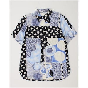 Puede incluir: Camisa abotonada de manga corta con diseño patchwork. La camisa presenta una mezcla de estampados, incluyendo lunares negros, círculos azules y blancos y espirales abstractos. La paleta de colores incluye negro, blanco y varias tonalidades de azul.