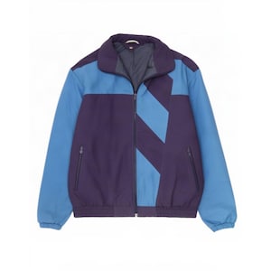 May include: A zip-up jacket featuring a color-blocked design in dark purple and light blue. The jacket has a high collar, long sleeves with elastic cuffs, and two side pockets with zipper closures. The front displays a diagonal light blue stripe.