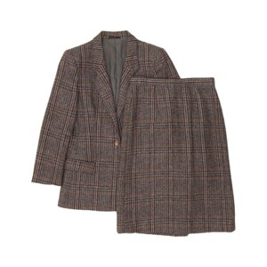 May include: A two-piece suit set consisting of a long-sleeve blazer and a matching skirt. Both pieces feature a brown, grey, and dark red plaid pattern. The blazer has a notched lapel, a single front button closure, and two front flap pockets.
