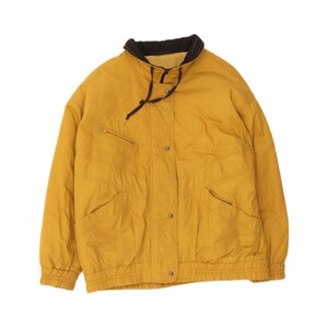 May include: A mustard yellow jacket featuring a high collar with a black interior lining and black drawstring cords. The jacket includes a front zipper closure, a snap button placket, two side pockets, and a small zippered chest pocket.