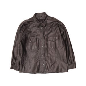 May include: A dark brown leather shirt featuring a pointed collar, long sleeves with buttoned cuffs, and a front button-down closure. The garment includes two chest pockets with flaps and snap buttons, along with horizontal seam detailing.