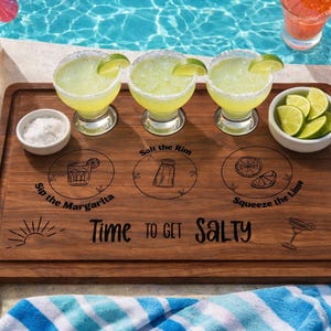 May include: A wooden serving tray with three margarita cocktails, salt, and lime slices. The tray has the text "Time to Get Salty" and instructions for making margaritas. Yellow flip-flops and a striped towel are also visible.