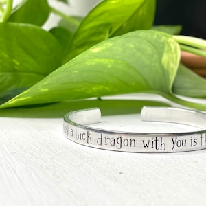 Op de afbeelding: Zilveren armband met de inscriptie "Carrying a luck dragon with you is the only", een populaire quote uit de animatiefilm Hoe tem je een draak.