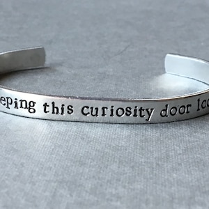 Puede incluir: Pulsera de brazalete de plata con la inscripción "Are you keeping this curiosity door locked?"