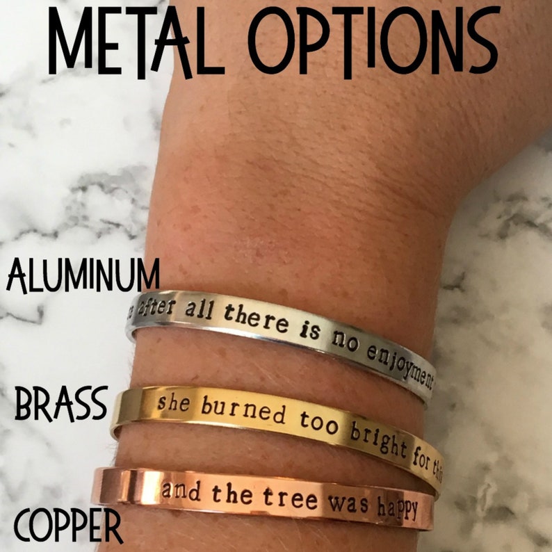 May include: Three metal bracelets with different inscriptions. The top bracelet is silver and says "after all there is no enjoyment". The middle bracelet is gold and says "she burned too bright for the". The bottom bracelet is copper and says "and the tree was happy".