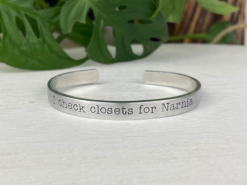 May include: A silver metal bracelet with the inscription "I check closets for Narnia".