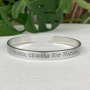 May include: A silver bracelet with the inscription "I check closets for Narnia".