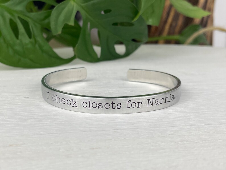 May include: A silver bracelet with the inscription "I check closets for Narnia".