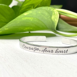 May include: Silver bangle bracelet inscribed with the words "Courage, dear heart".
