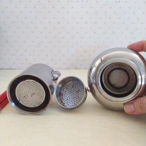 May include: A silver coffee maker with a removable filter and a lid. The coffee maker is disassembled, showing the interior of the pot and the filter.