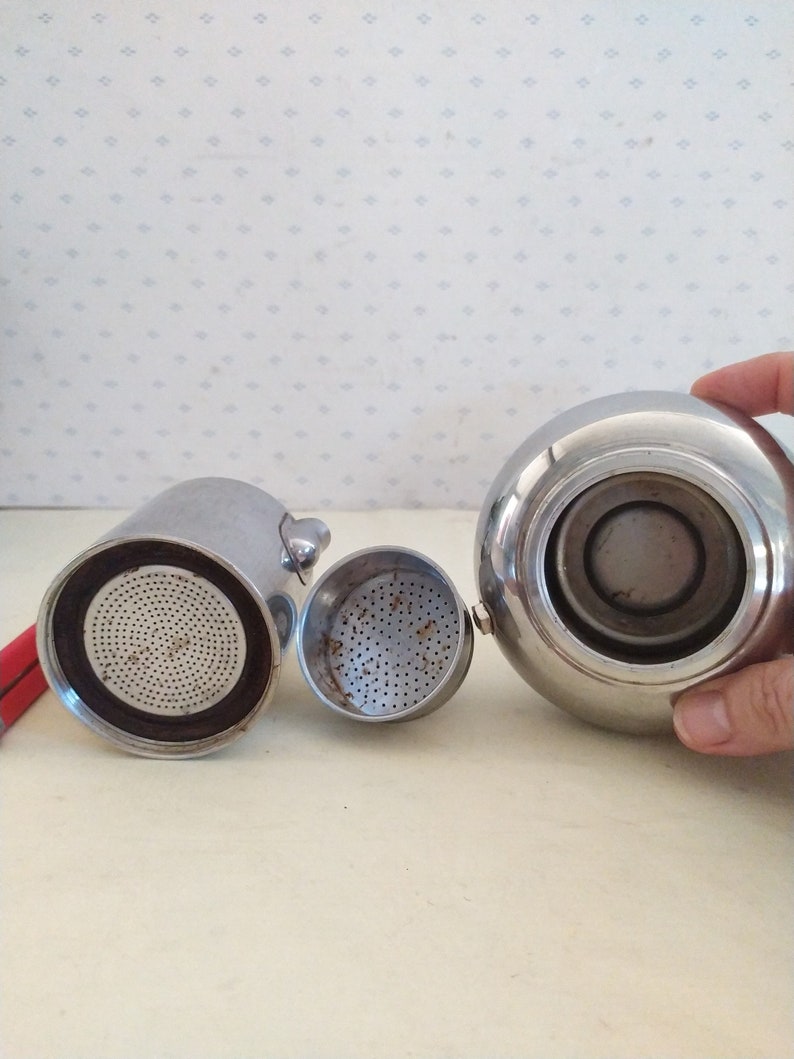May include: A silver coffee maker with a removable filter and a lid. The coffee maker is disassembled, showing the interior of the pot and the filter.
