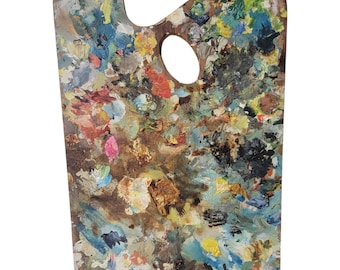 May include: A well-used wooden artist's palette, rectangular with a thumb hole. The palette is covered in a variety of dried paint colors, including blue, yellow, red, and brown. The palette shows signs of wear and tear, indicating it has been used for painting.
