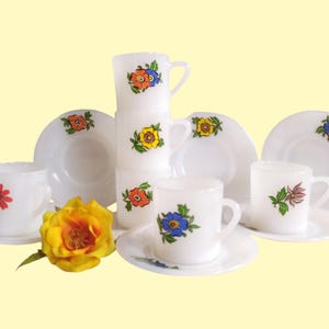 May include: Set of six white ceramic coffee cups and saucers with floral designs in shades of blue, red, yellow, and green.