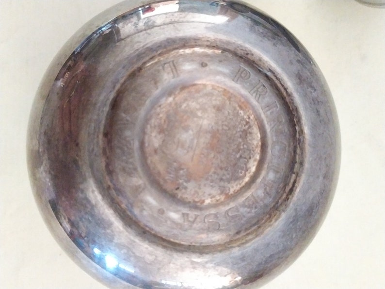 May include: Close-up of the bottom of a silver-plated cup with the words "PRINCESS" and "USA" engraved on the bottom.