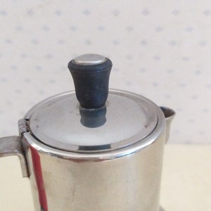 May include: A silver stainless steel coffee pot with a black plastic lid knob.