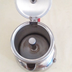 May include: A silver metal stovetop espresso maker with a removable lid. The lid is open and the inside of the maker is visible.