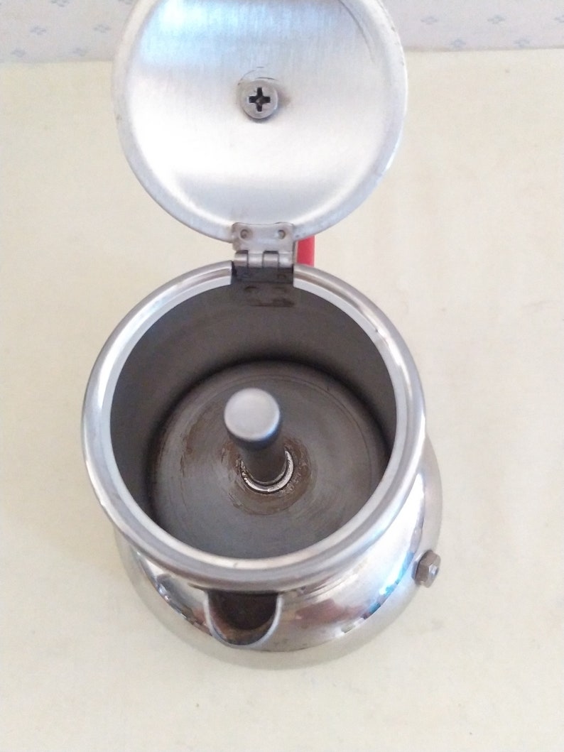 May include: A silver metal stovetop espresso maker with a removable lid. The lid is open and the inside of the maker is visible.