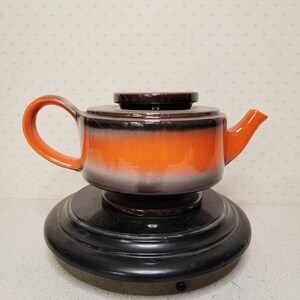 Peut inclure: Théière en céramique avec un glaçage dégradé orange et marron, avec un couvercle et une anse assortis. La théière repose sur une base noire circulaire. Design vintage, idéal pour servir le thé.