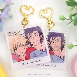 Könnte beinhalten: Zwei transparente Acryl-Schlüsselanhänger mit goldenen herzförmigen Verschlüssen. Jeder Schlüsselanhänger zeigt ein Foto von zwei Anime-Charakteren, Cloud und Zack, mit dem Text "Cloud and Zack" unter dem Foto.