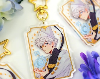 May include: A rectangular acrylic keychain featuring an illustration of a white-haired character in a white hat and cape with gold buttons, holding a glowing blue orb. The keychain has a gold star-shaped clasp and the text shop.sarafabrizi.com.