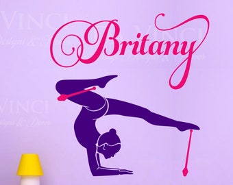 May include: A purple vinyl wall decal featuring a gymnast in a handstand with a ribbon. The name "Brittany" is written in pink script above the gymnast. The wall art includes the text "DA VINCI Vinyl Designs & Decor".